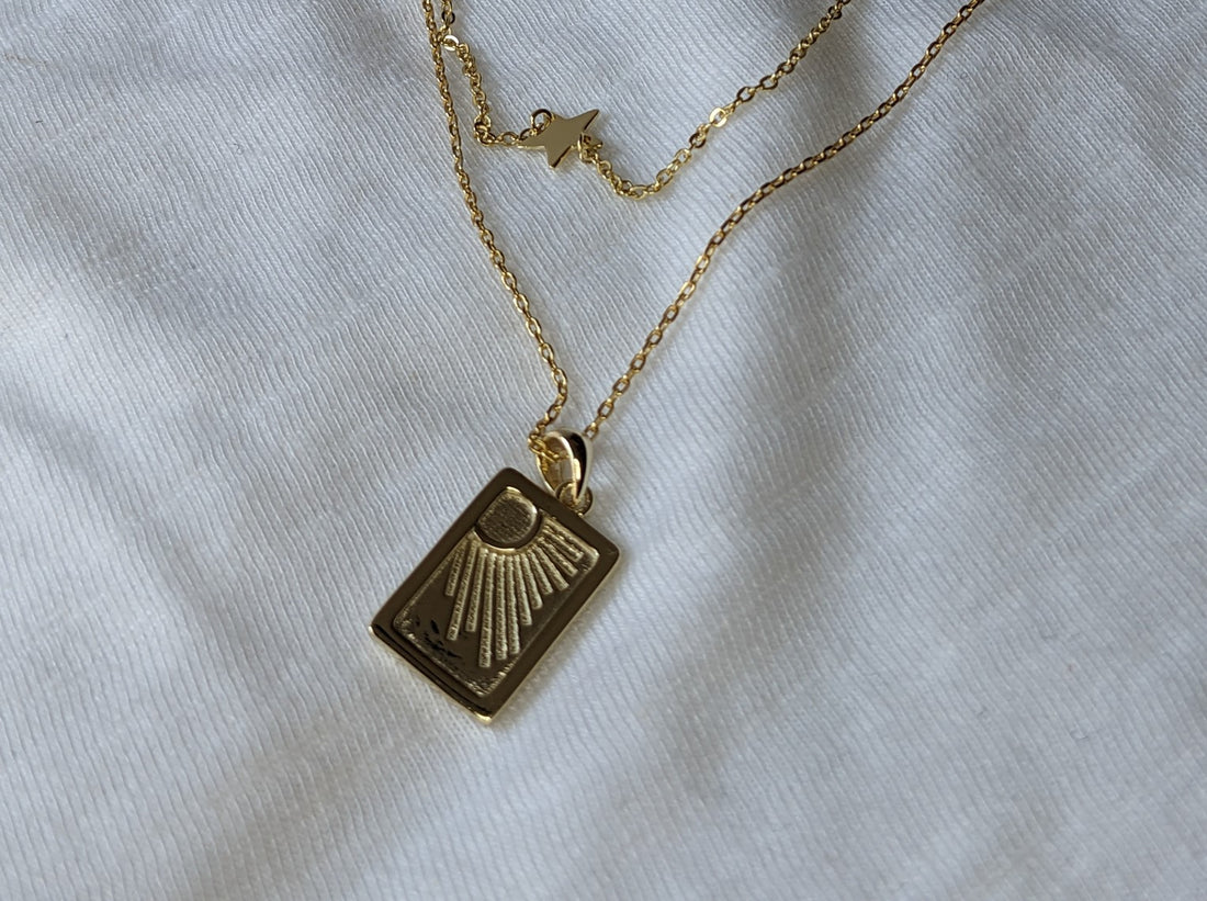 Image of a gold necklace with an oblong pendant with a sun shining rays of sunlight down